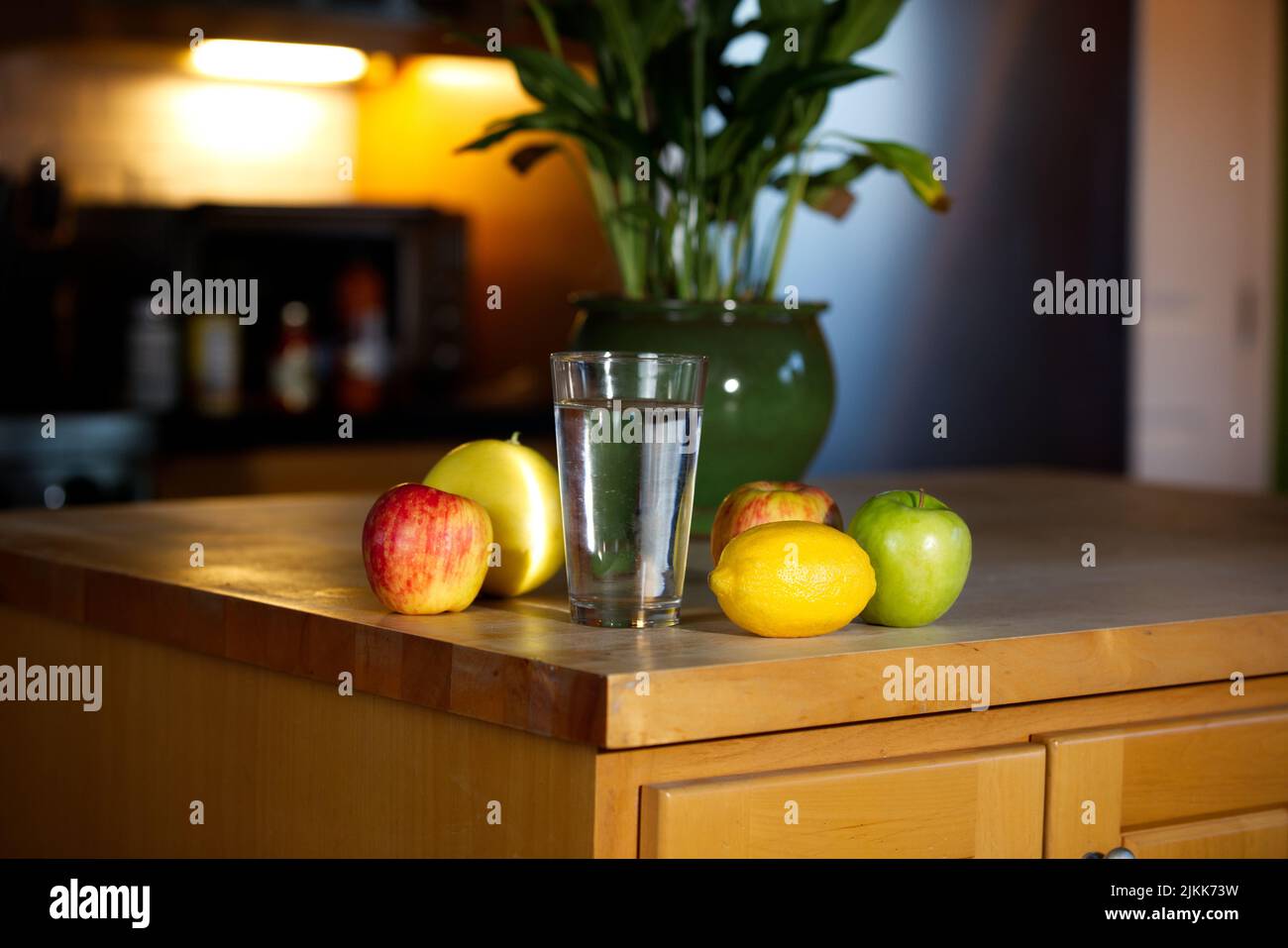 Ein Glas Wasser und Früchte auf einem Holztisch vor dem verschwommenen Hintergrund einer Topfpflanze Stockfoto
