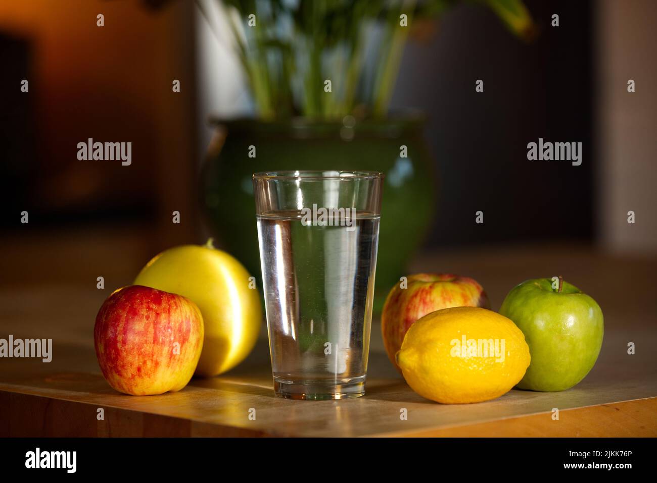 Eine Nahaufnahme von Glaswasser und Früchten auf einem Holztisch vor dem verschwommenen Hintergrund einer Topfpflanze Stockfoto