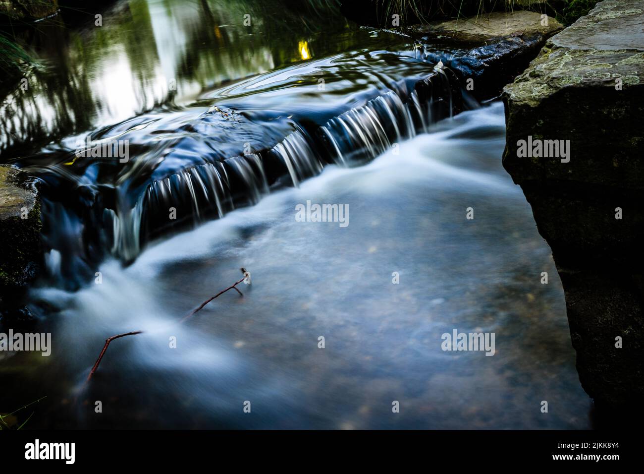 Nahaufnahme eines kleinen Wasserfalls, der flussabwärts in einen Wald fließt, mit langer Belichtung Stockfoto