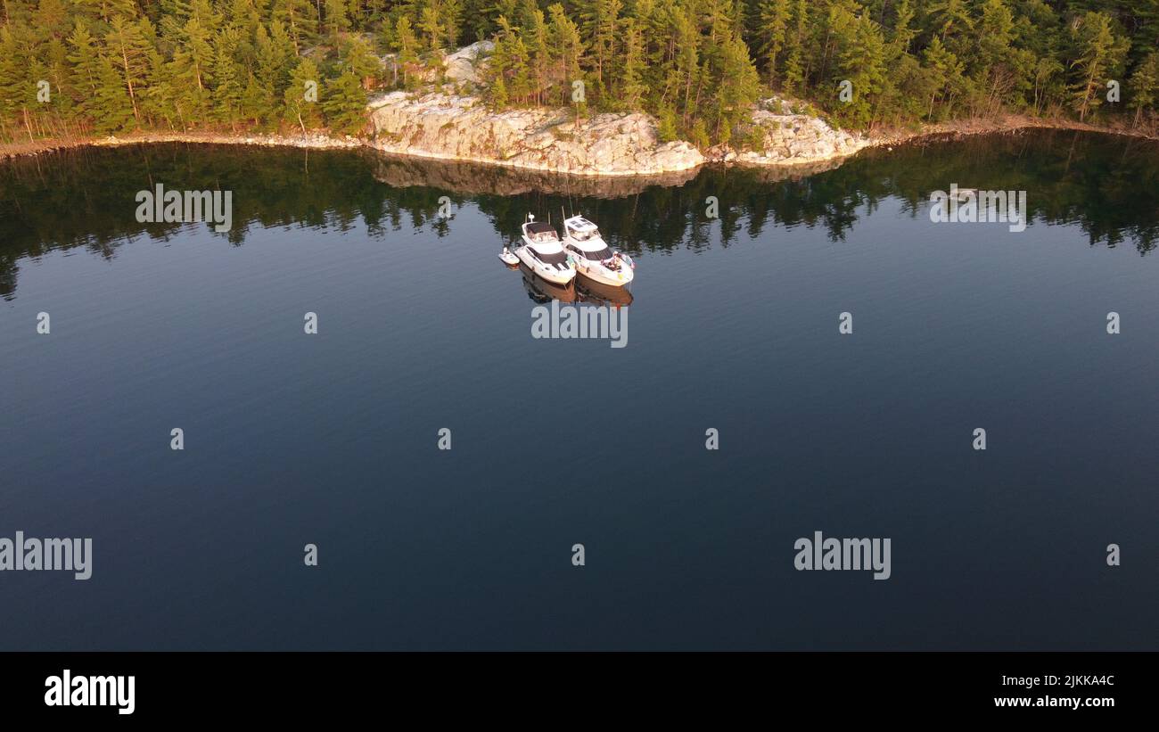 Eine Vogelperspektive auf einen See, der die Bäume der Küste reflektiert, mit zwei Booten darauf Stockfoto