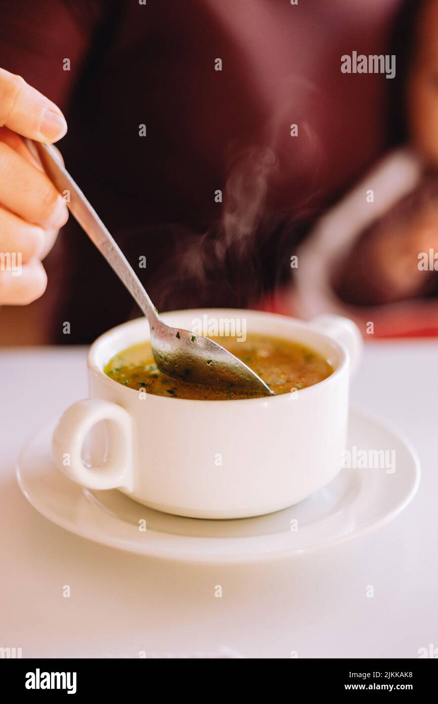 Eine vertikale Aufnahme einer Person, die eine heiße, dampfende Suppe mit Gemüse in einem Keramikaufsatz isst Stockfoto
