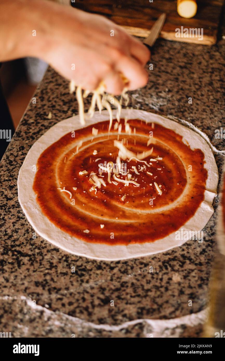 Eine Hand bestreuen geriebenen Käse zu einer Pizza Stockfoto