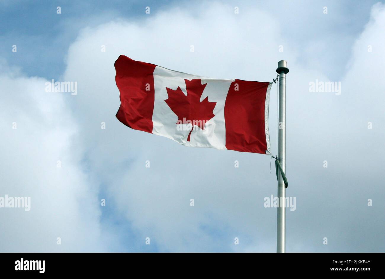 Eine wunderschöne Aufnahme der kanadischen Flagge, die mit weißen Wolken im Hintergrund des Himmels winkt Stockfoto