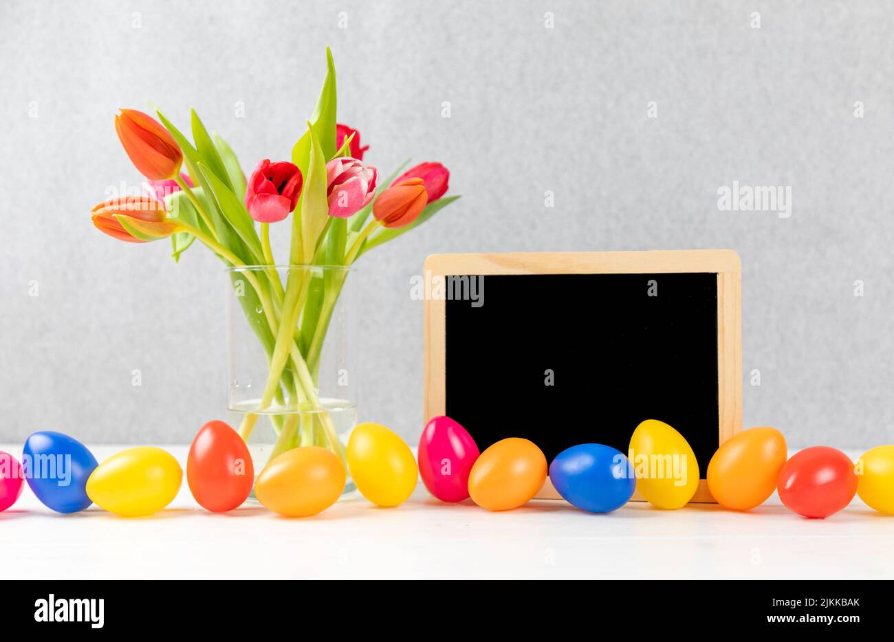 Bunte Tulpen mit Kreidetafel und ostereiern auf grauem Hintergrund Stockfoto