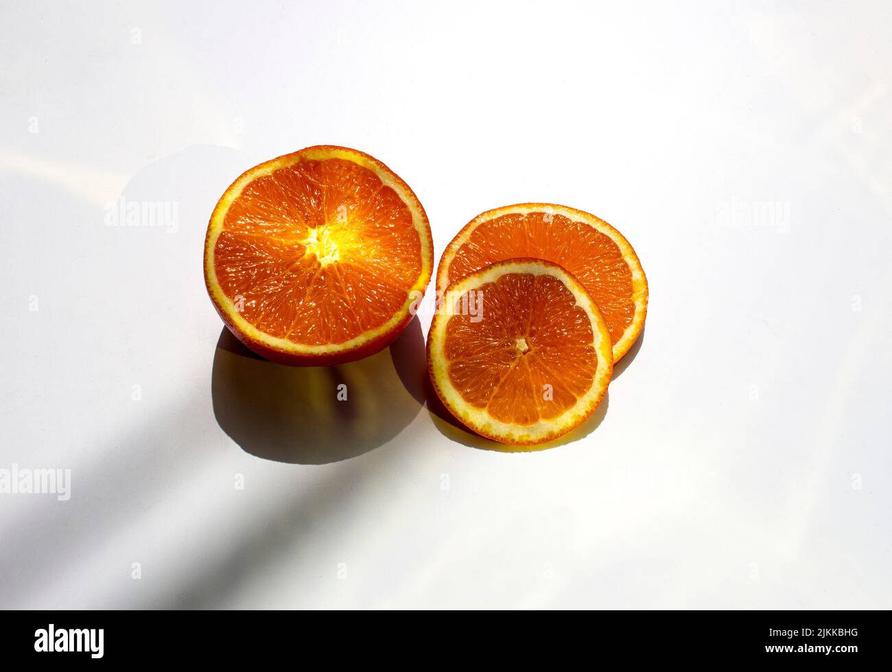 Eine Nahaufnahme von reifen, saftigen Orangenscheiben auf weißem Hintergrund mit Schatten von Blättern Stockfoto