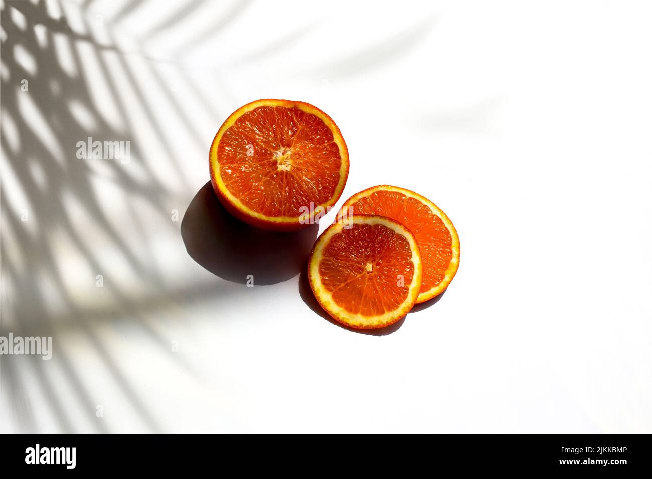 Eine Nahaufnahme von reifen, saftigen Orangenscheiben auf weißem Hintergrund mit Schatten von Blättern Stockfoto
