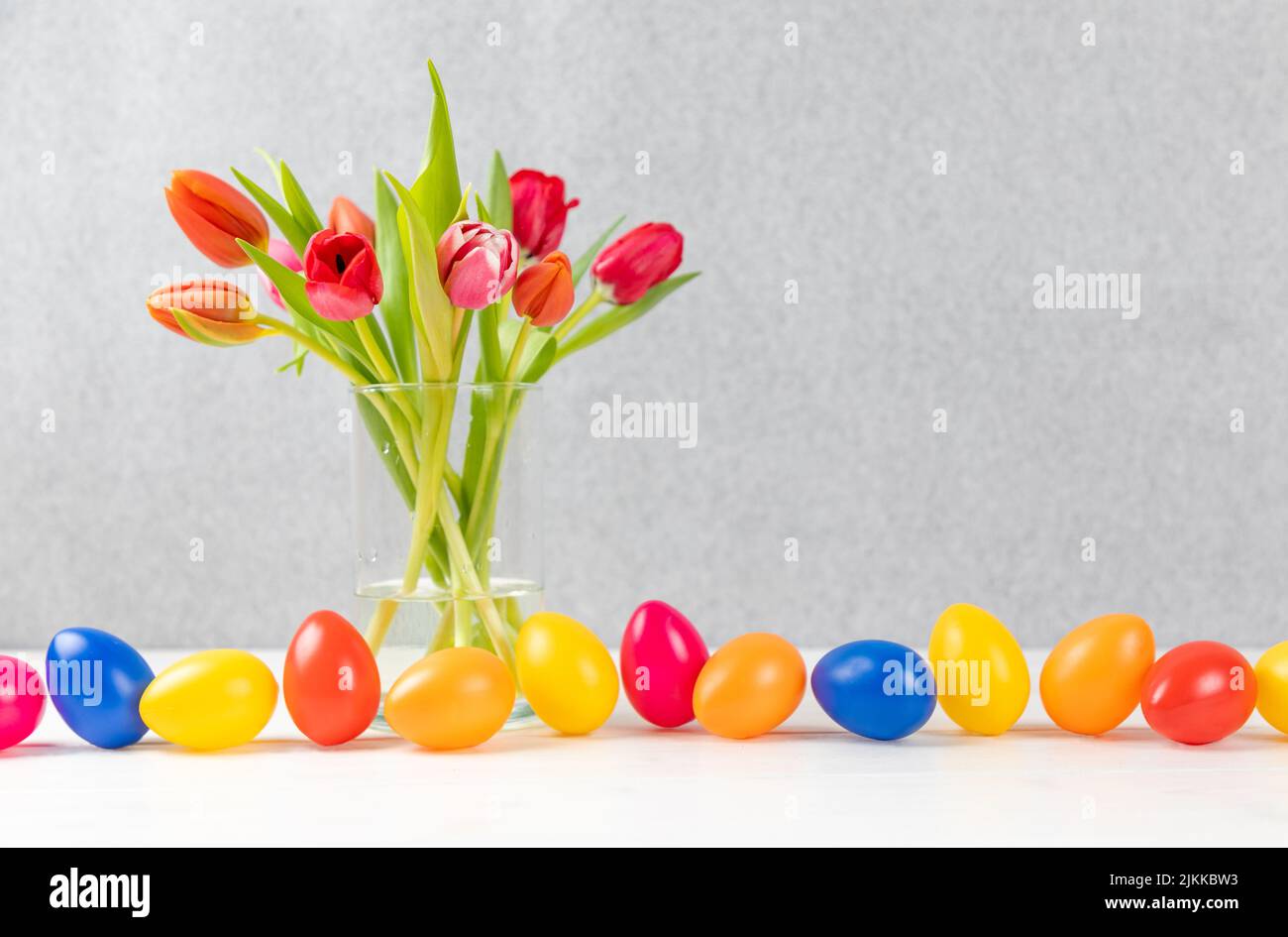 Eine Nahaufnahme eines Tulpenstraußes in einer Vase in der Nähe von farbenfrohem ostereiss Stockfoto