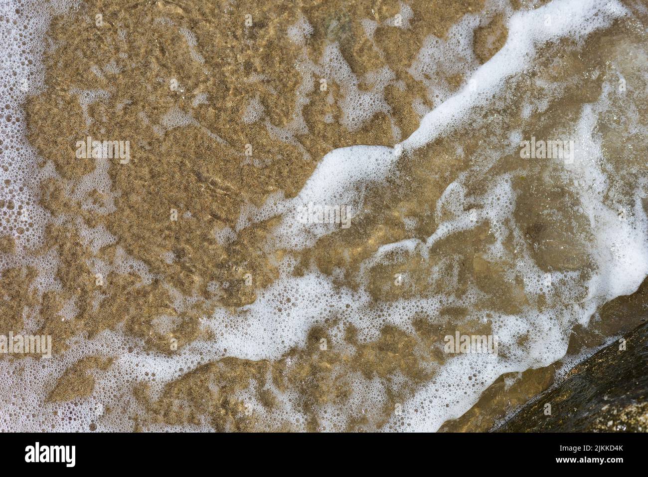 Strand Sand Meer Wasser Sommer Hintergrund. Sand Strand Wüste Textur. Blick von oben auf die weiße Schaumwelle und die sandige Küste Stockfoto