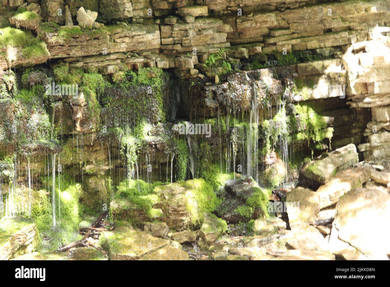 Ein künstlicher Wasserfall, der auf moosigen Felsen in einem grünen Park fließt Stockfoto