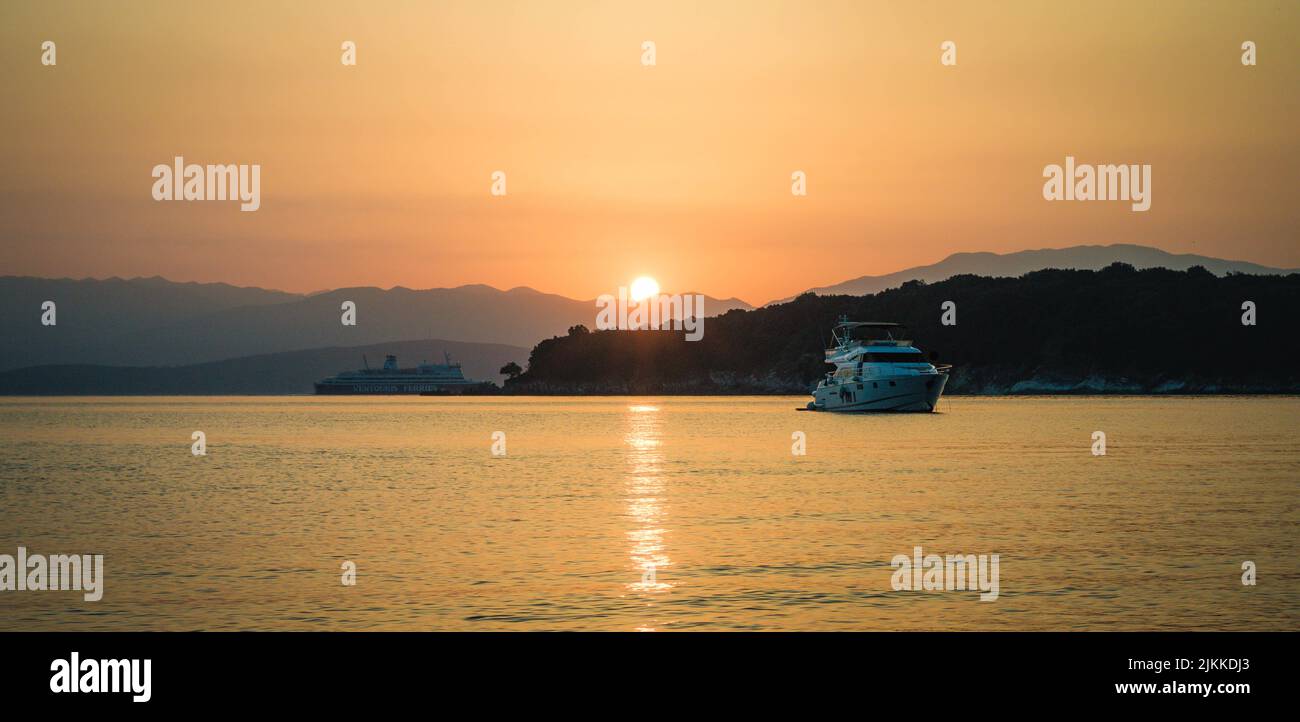 Eine malerische Aussicht auf Boote, die bei Sonnenuntergang gegen die mit viel Grün bedeckten Hügel segeln Stockfoto