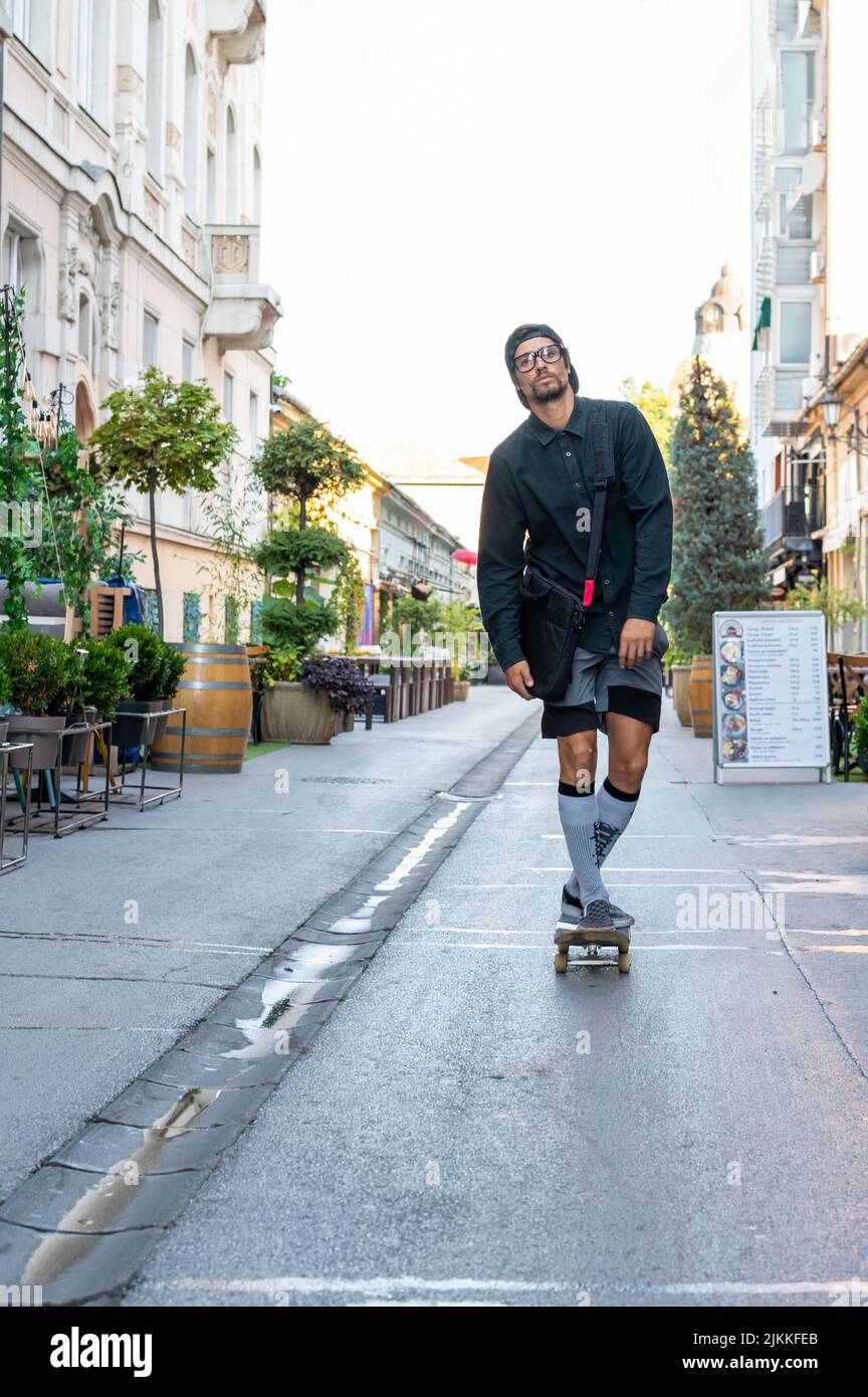 Eine schöne Aufnahme eines erwachsenen kaukasischen Mannes, der an einem sonnigen Tag auf der Straße Skateboarding fährt Stockfoto