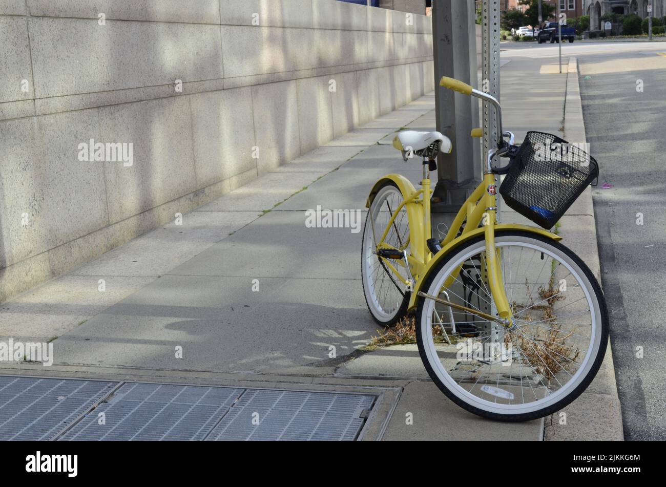 Eine niedliche Aufnahme eines gelben Fahrrads, das auf einer Stange in einer sauberen Straße neben der Straße gelehnt ist Stockfoto