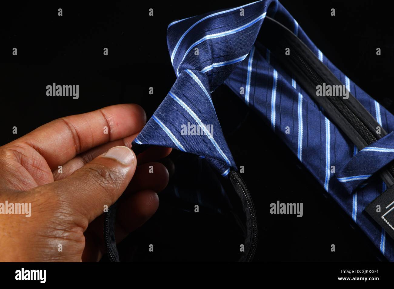 Eine Hand, die eine Krawatte auf schwarzem Hintergrund hält Stockfoto