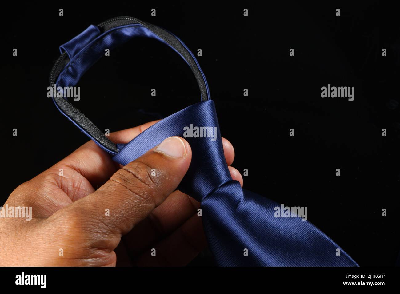 Eine Hand hält eine Krawatte isoliert auf schwarzem Hintergrund Stockfoto