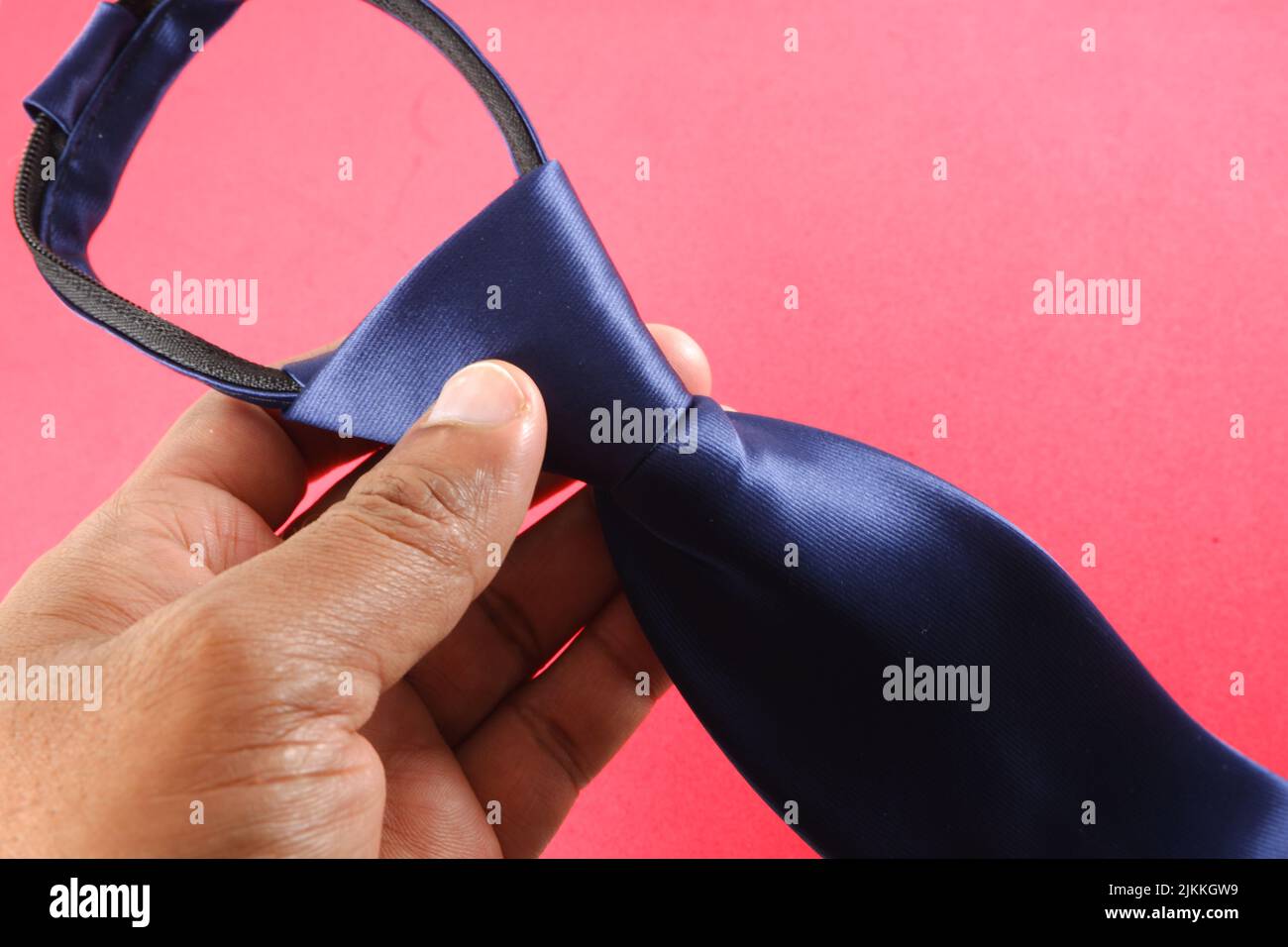 Eine Hand, die eine blaue Krawatte auf einem rosa Hintergrund hält Stockfoto