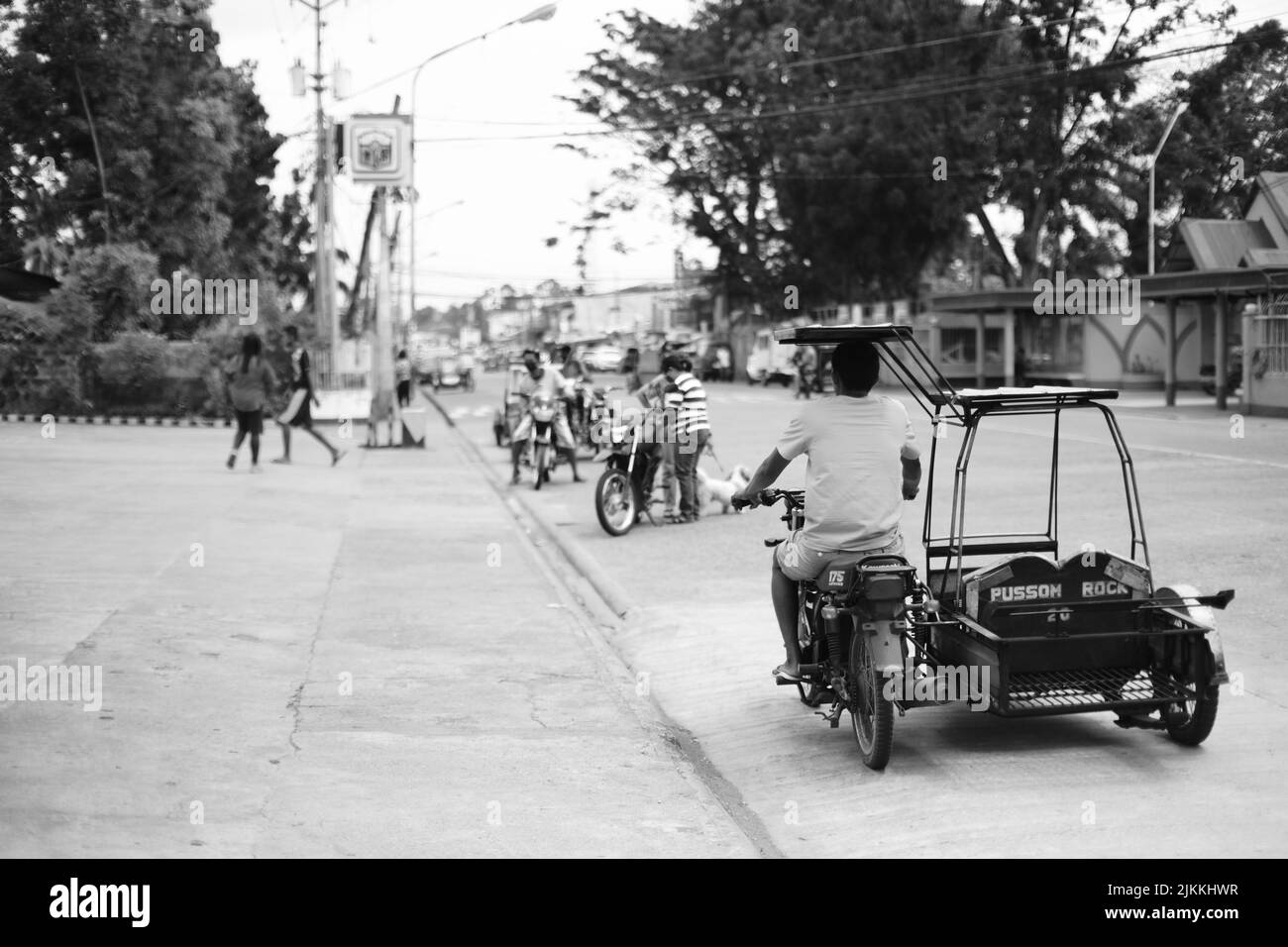Eine Graustufenaufnahme von Menschen, die auf den Philippinen die Straße entlang fahren, mit Grün auf der Straße Stockfoto