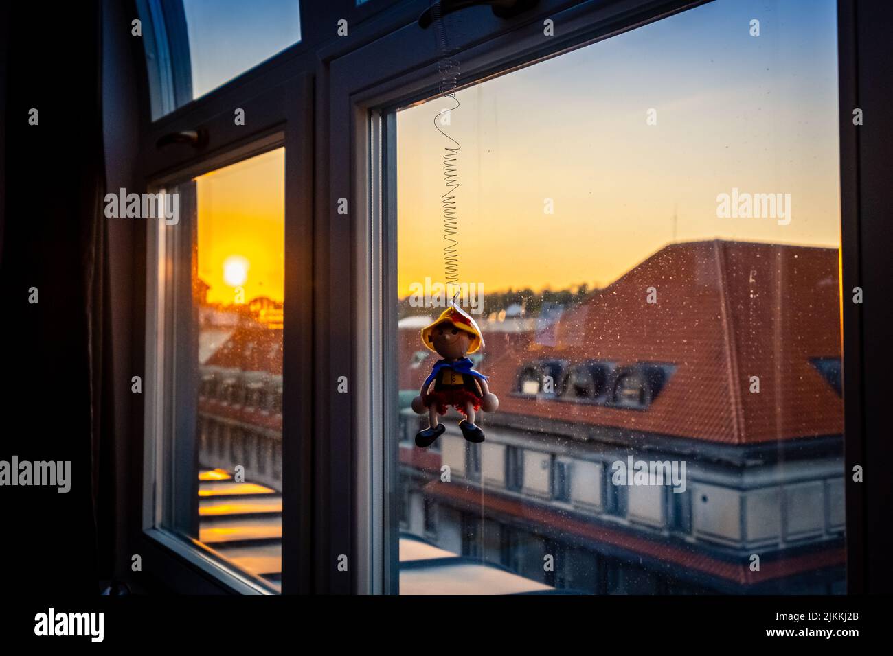 Eine Nahaufnahme einer kleinen Pinoccio-Puppe, die an einem Fenster hängt, mit Blick auf den Sonnenuntergang Stockfoto