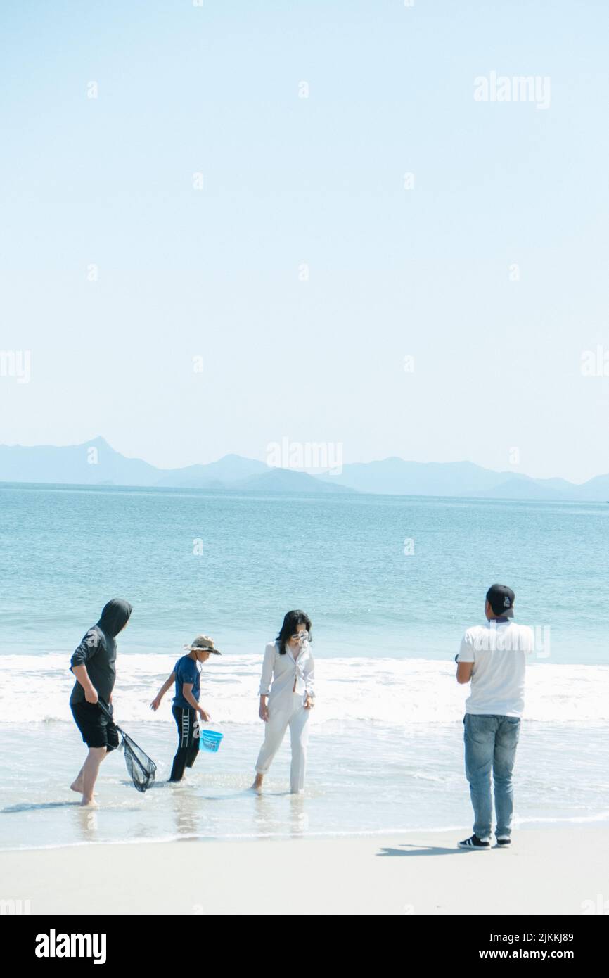 Zwei Personen mit einem Netz und einem Eimer hinter einer Frau, die während des Fotoshootings am Strand posiert Stockfoto