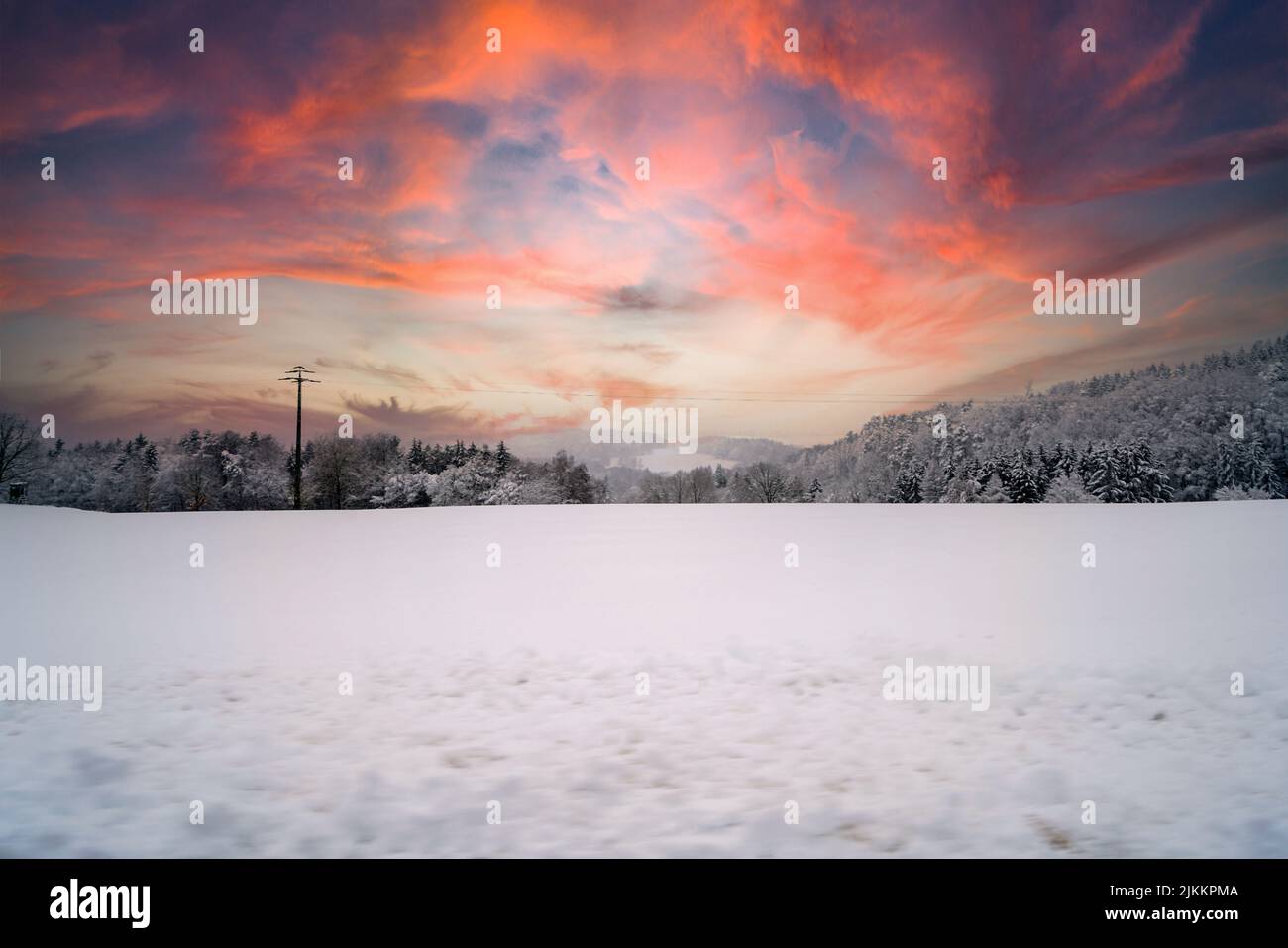 Der faszinierende Sonnenuntergang Schnee über dem schneebedeckten Feld mit einem Wald weit entfernt gesehen Stockfoto
