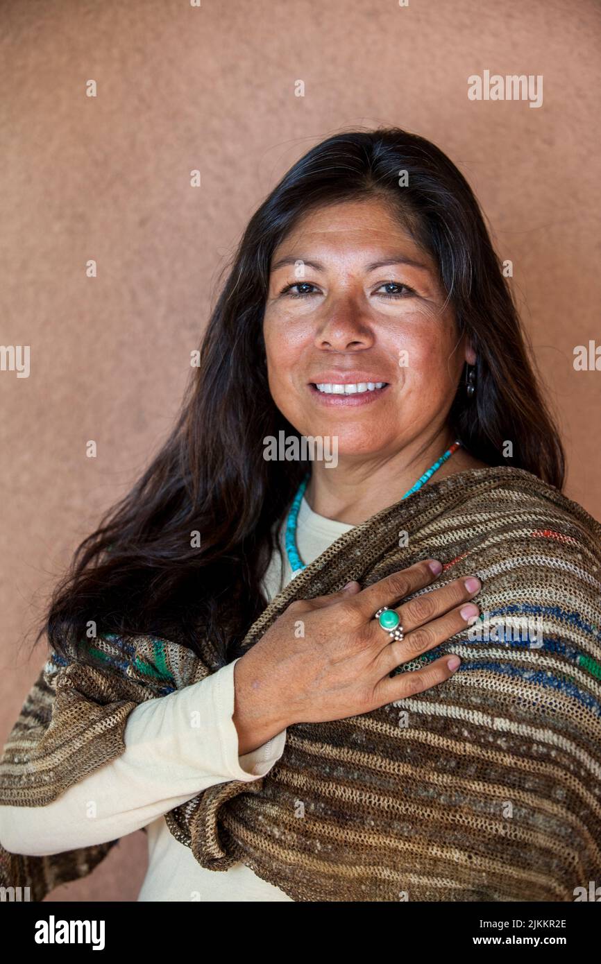 Isleta Pueblo Frau in Schal und türkisfarbenen Perlen gekleidet legt ihre rechte Hand über ihr Herz neben adobe Wand. Santa Fe New Mexico Stockfoto