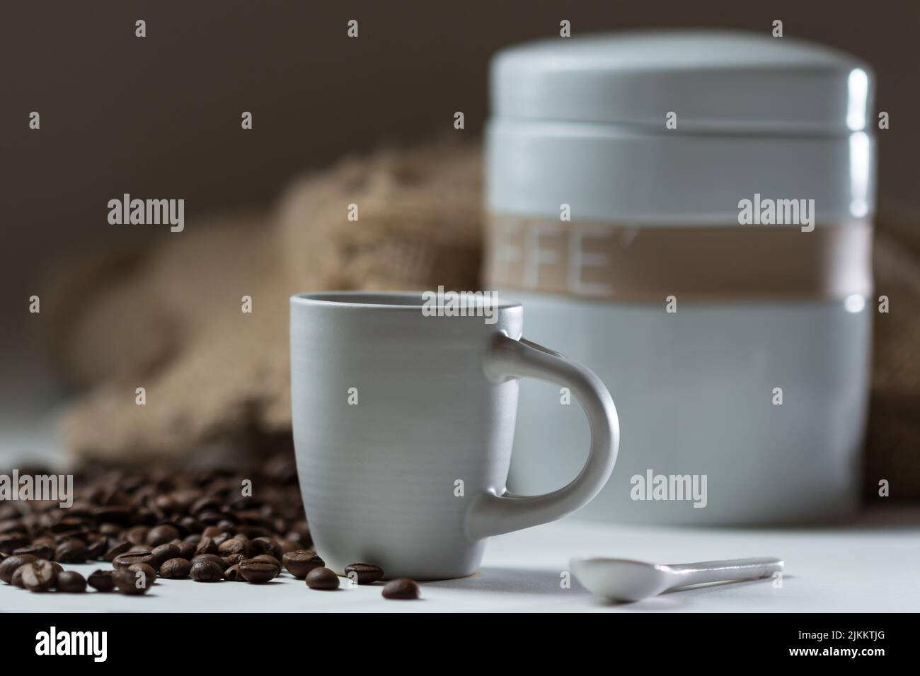 Ein flacher Fokus einer Tasse heißen Kaffees mit Kaffeebohnen und weißem Behälter im Hintergrund Stockfoto