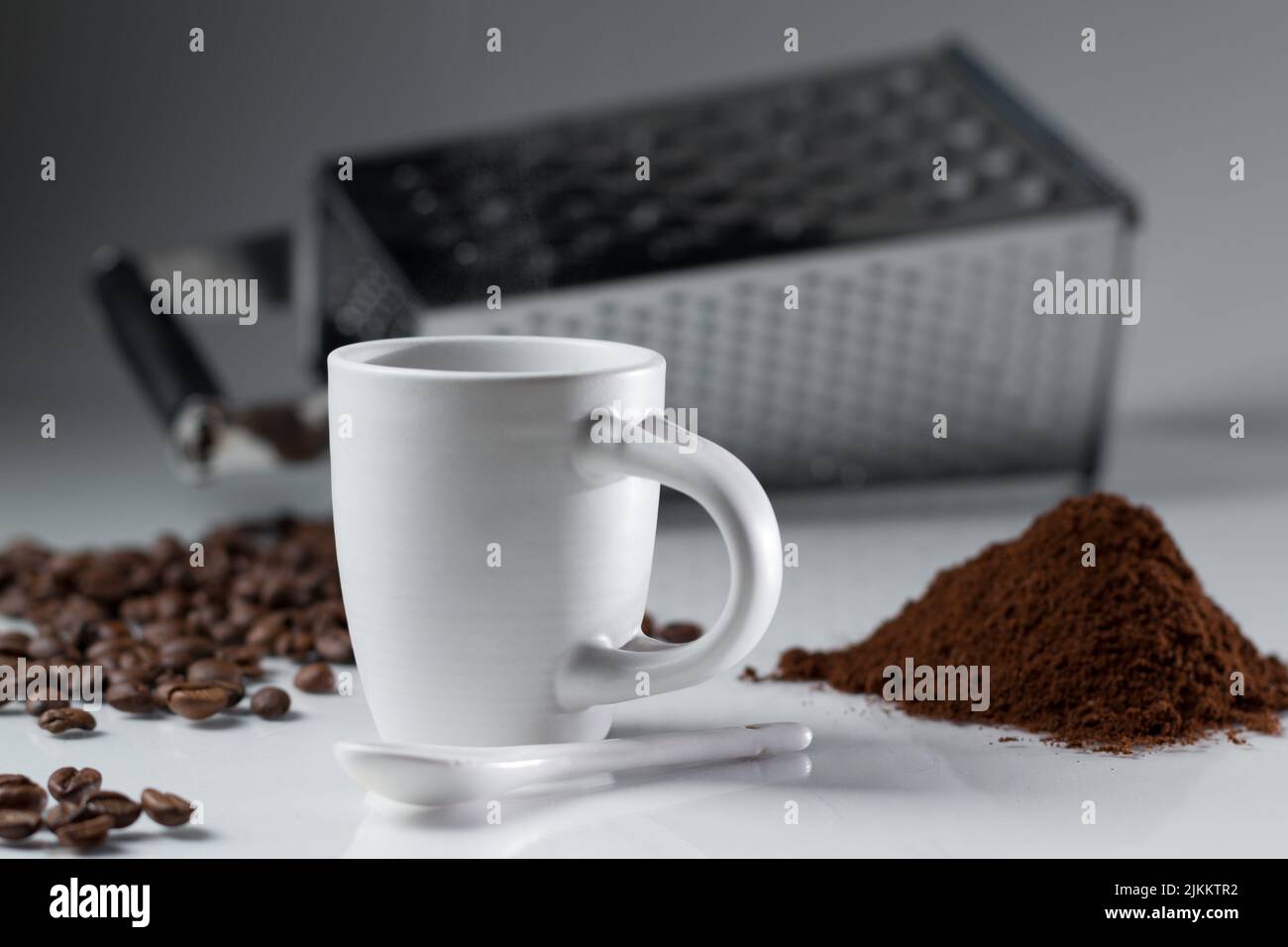 Ein flacher Fokus einer weißen Kaffeetasse mit Kaffeebohnen und Pulver mit einer Reibe auf dem Hintergrund Stockfoto