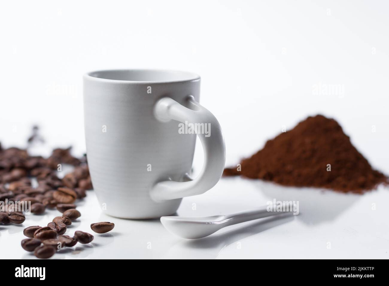 Ein flacher Fokus einer weißen Kaffeetasse mit Kaffeebohnen und Pulver auf weißem Hintergrund Stockfoto