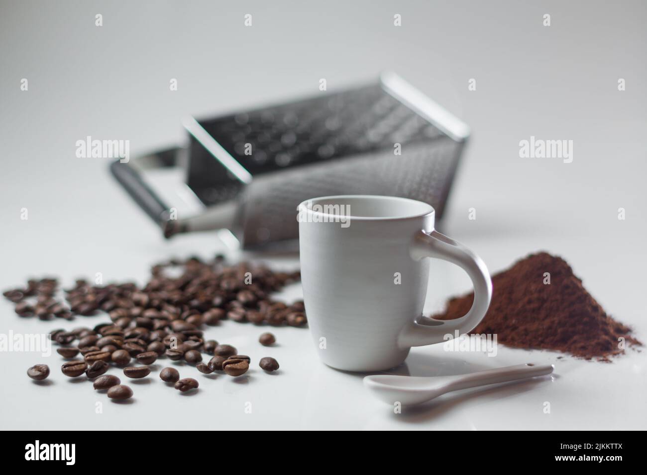 Ein flacher Fokus einer weißen Kaffeetasse mit Kaffeebohnen und Pulver mit einer Reibe auf dem Hintergrund Stockfoto