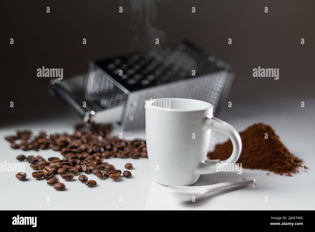 Ein flacher Fokus einer weißen Kaffeetasse mit Kaffeebohnen und Pulver mit einer Reibe auf dem Hintergrund Stockfoto