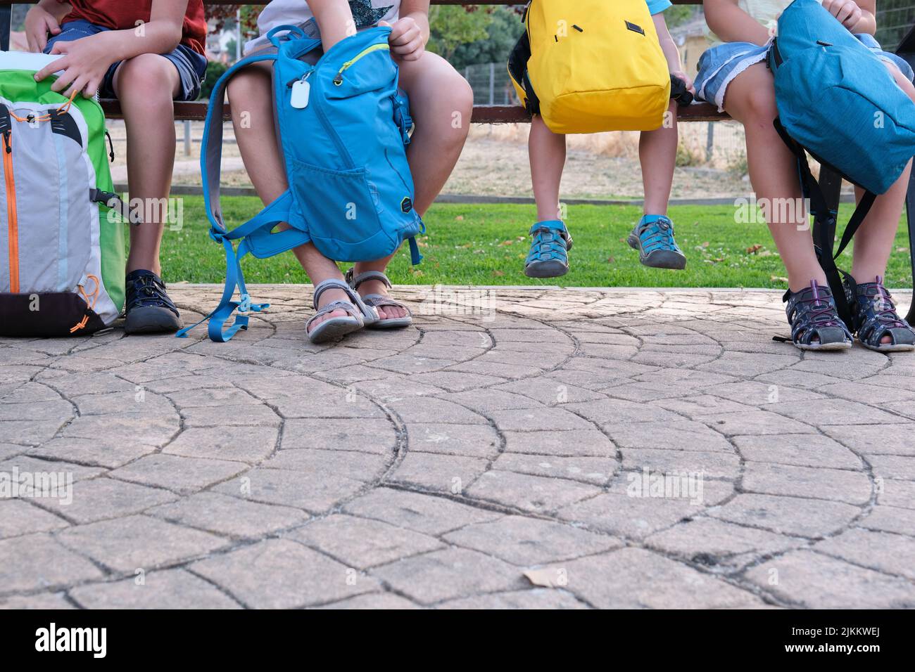 Beschnittenes Bild von Schulkindern, die mit ihren Rucksäcken auf einer Bank sitzen. Stockfoto