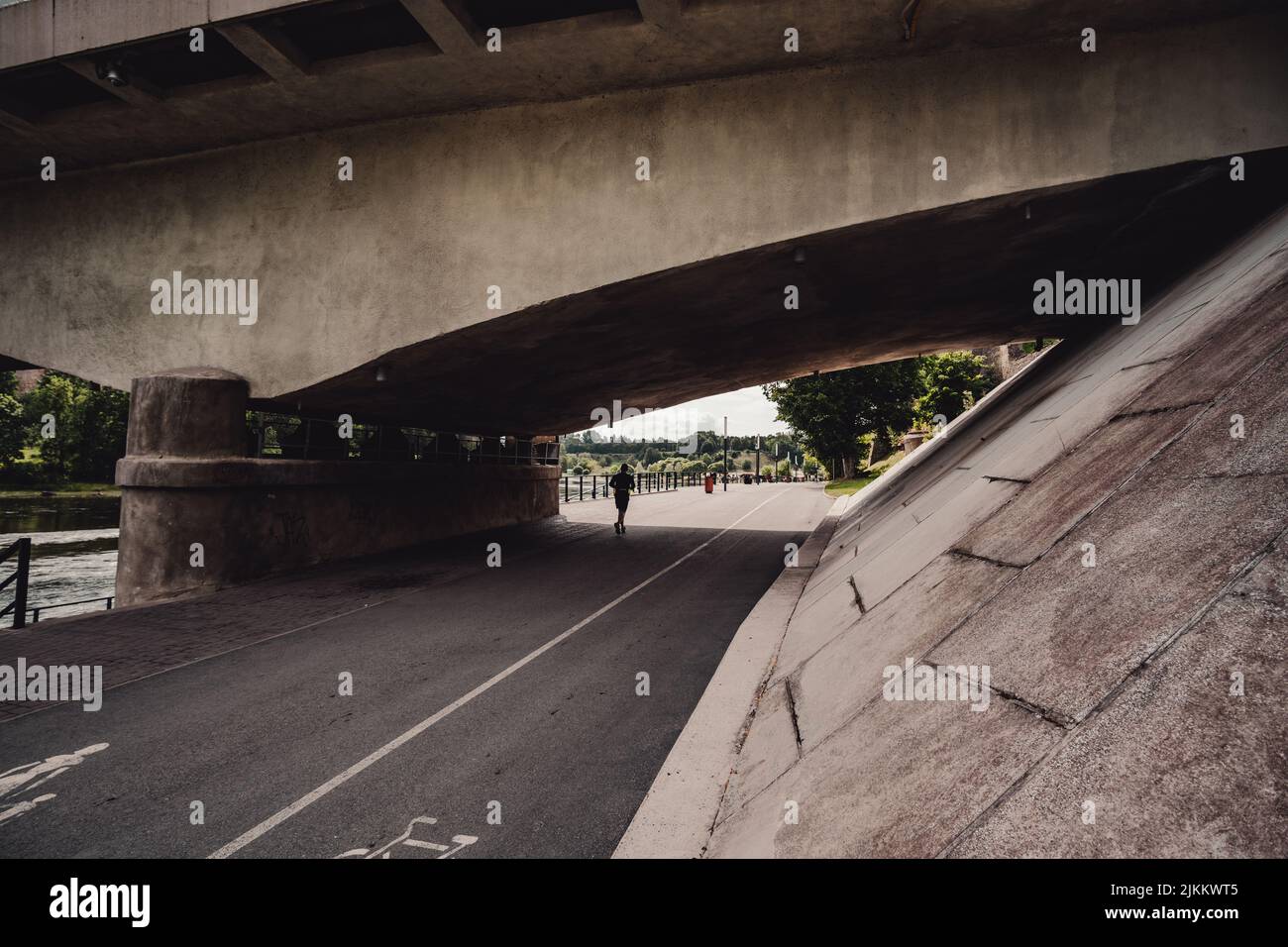 Blick auf eine Person, die tagsüber unter einer Brücke die Straße entlang läuft und Bäume in der Ferne hat Stockfoto