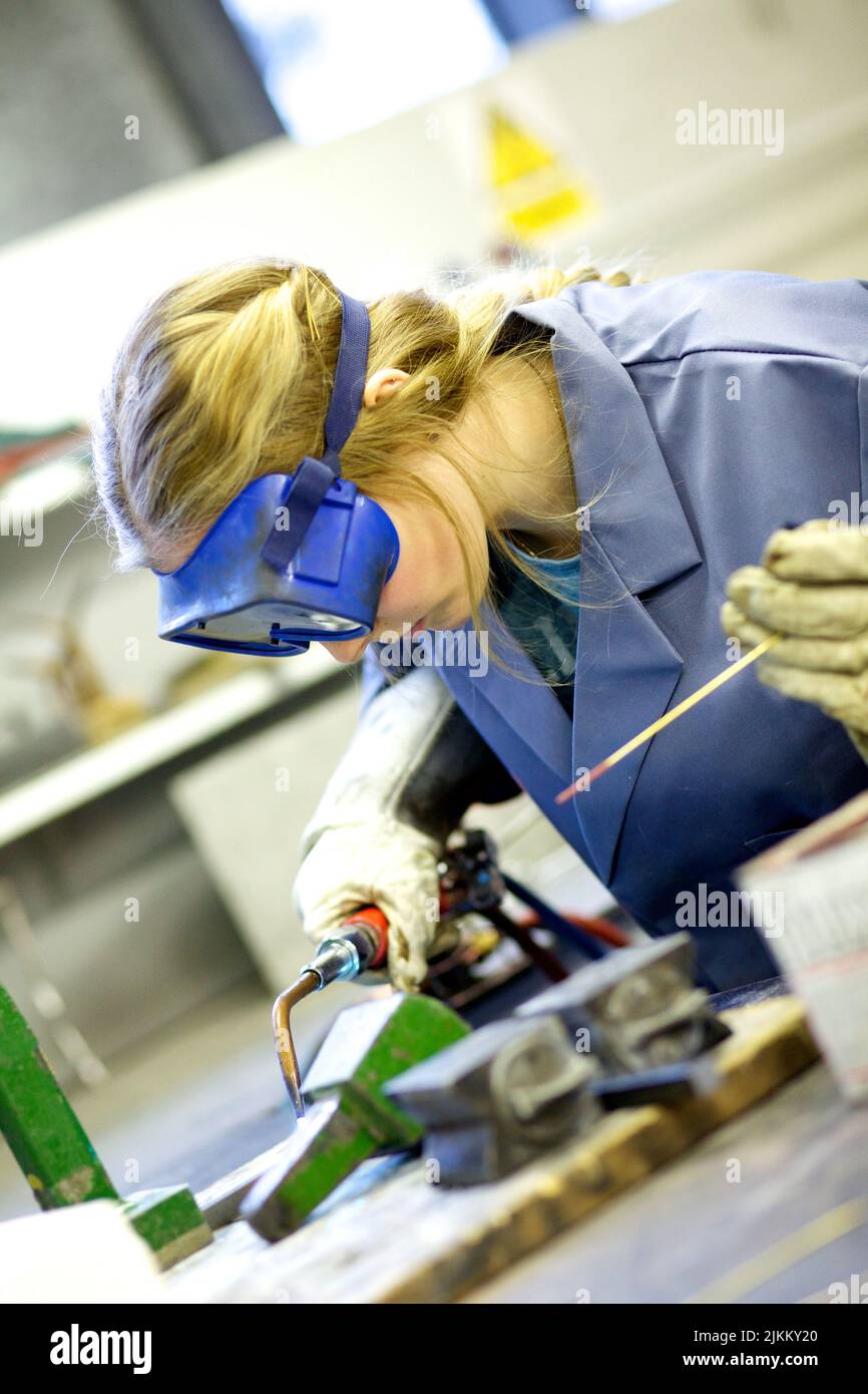 Eine Metallarbeiterin in einer Brille, die Stahl mit einem Blasbrenner schweißen soll Stockfoto
