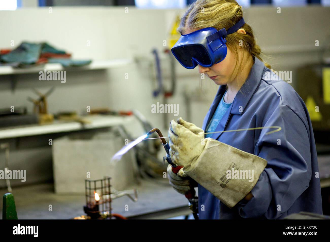 Eine Metallarbeiterin in einer Brille, die Stahl mit einem Blasbrenner schweißen soll Stockfoto