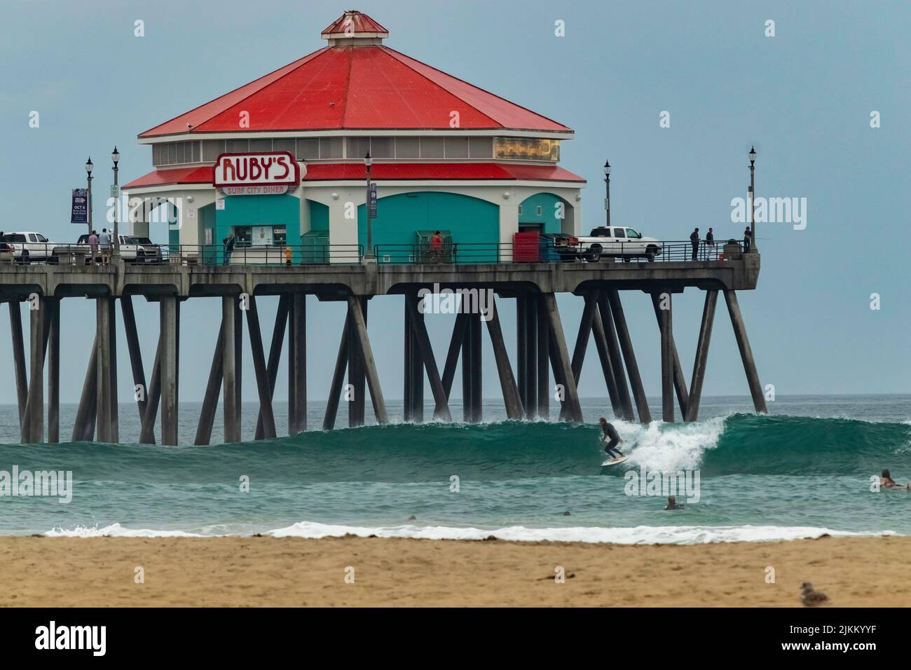 Ein malerischer Blick auf ein Ruby's Diner auf einem Pier über Menschen, die am Huntington Beach, Kalifornien, surfen Stockfoto