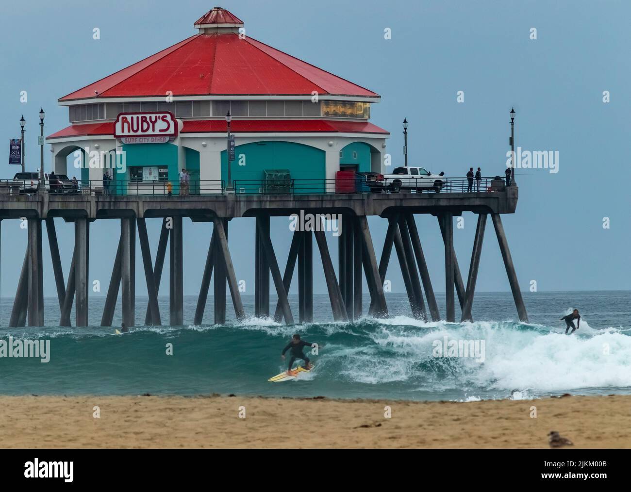 Ein malerischer Blick auf ein Ruby's Diner auf einem Pier über Menschen, die am Huntington Beach, Kalifornien, surfen Stockfoto