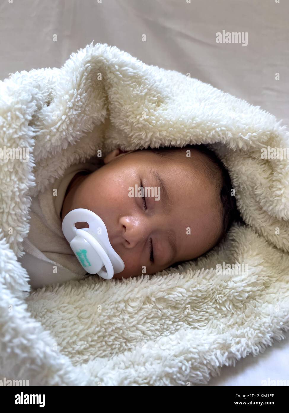 Süßes, friedliches Baby, das auf einem weißen Bettlaken liegt, genießt tagsüber Schlummer Stockfoto