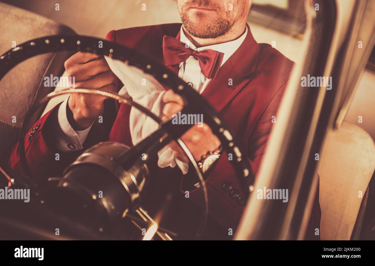 Elegante Männer tragen Fliege und Burgunder Siut hinter Classic Car Lenkrad. Stockfoto