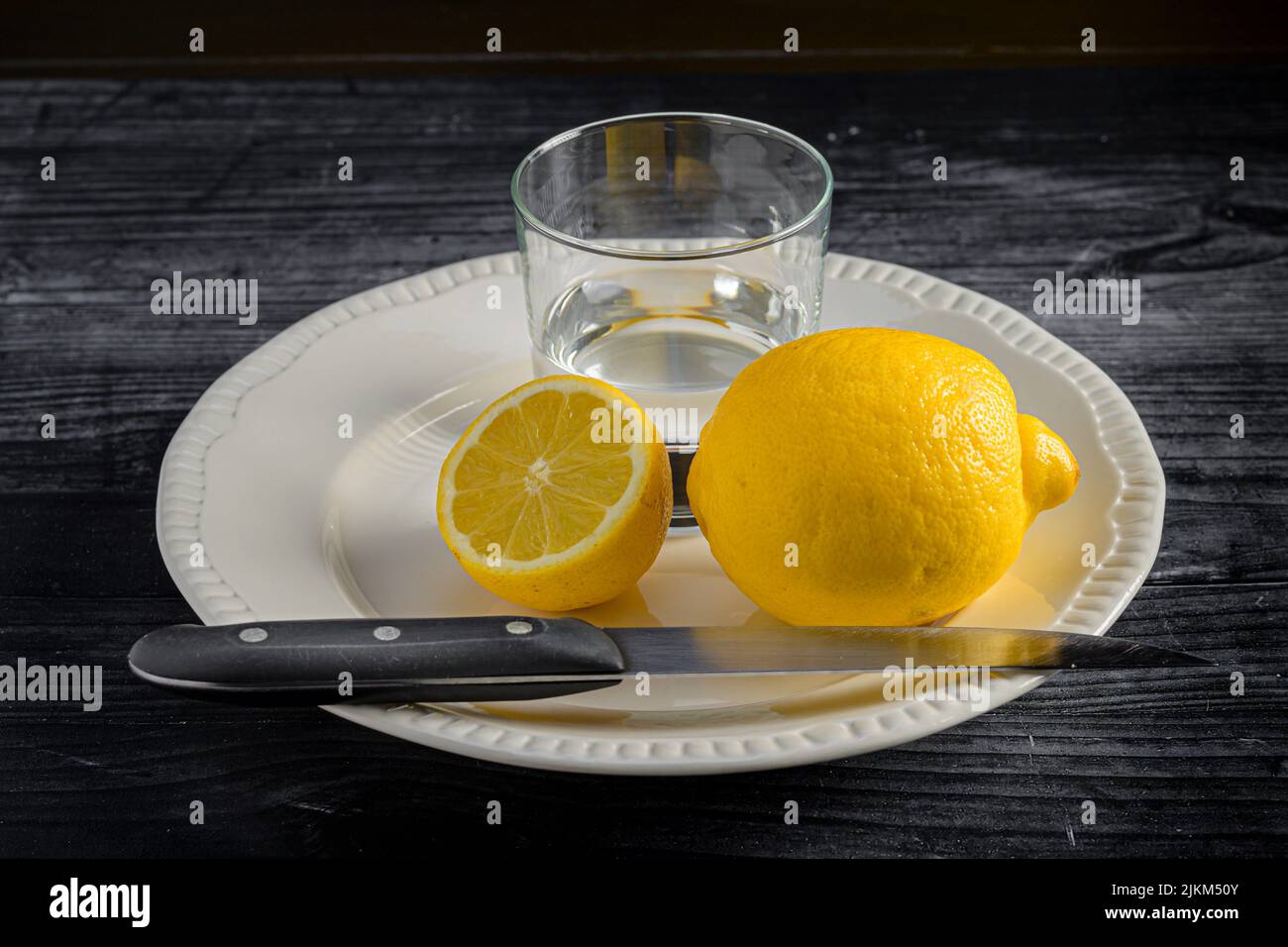 Ein Schuss Zitrone mit einem Glas Wasser in der Platte Stockfoto