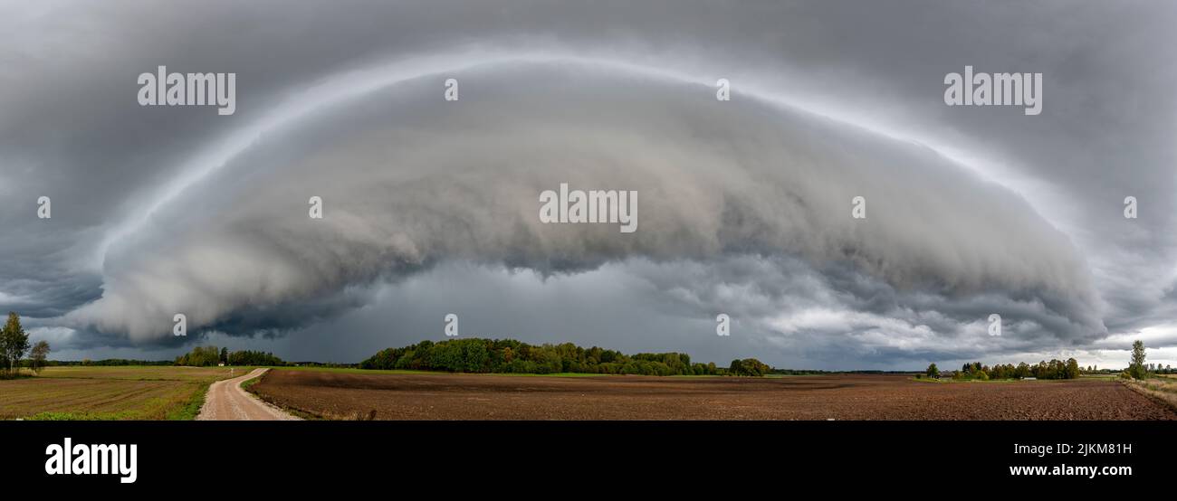 Eine Panoramaaufnahme von grauen, stürmischen Wolken über einer grünen, schönen Farm Stockfoto