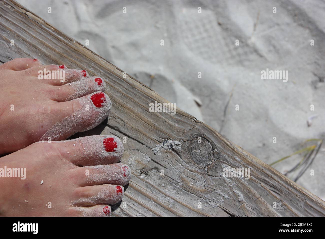 Eine Nahaufnahme der Füße einer Frau mit roter Maniküre, die auf Holz am Strand steht Stockfoto