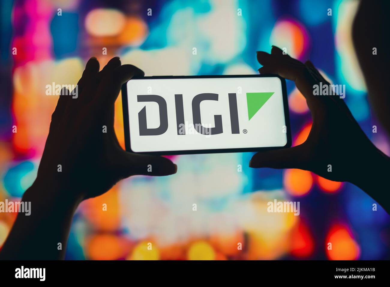 In dieser Abbildung hält eine Frau mit Silhouetten ein Smartphone mit dem Digi International-Logo auf dem Bildschirm. Stockfoto
