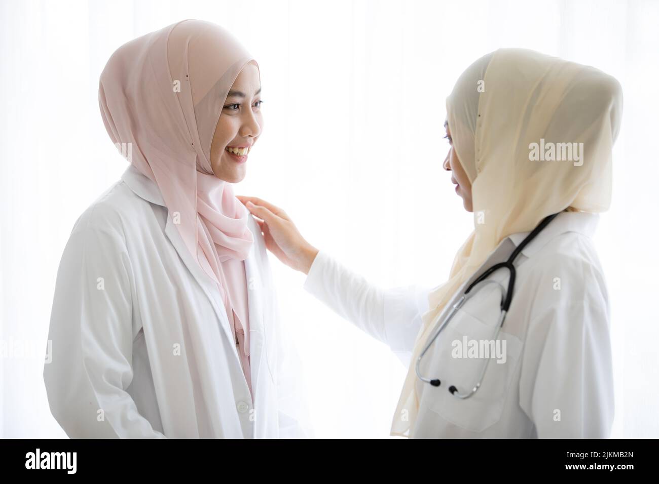 Zwei junge Thai-muslimische Ärztinnen unterhalten sich vor weißem Hintergrund Stockfoto