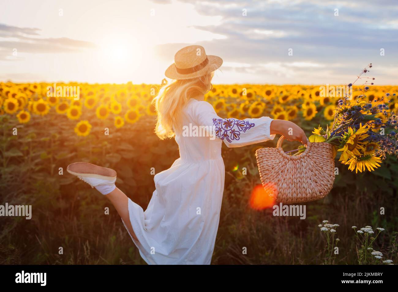 Glückliche Frau läuft in blühenden Sonnenblumenfeld bei Sonnenuntergang Spaß mit Tasche mit Blumen halten. Sommerzeit in der Ukraine Stockfoto