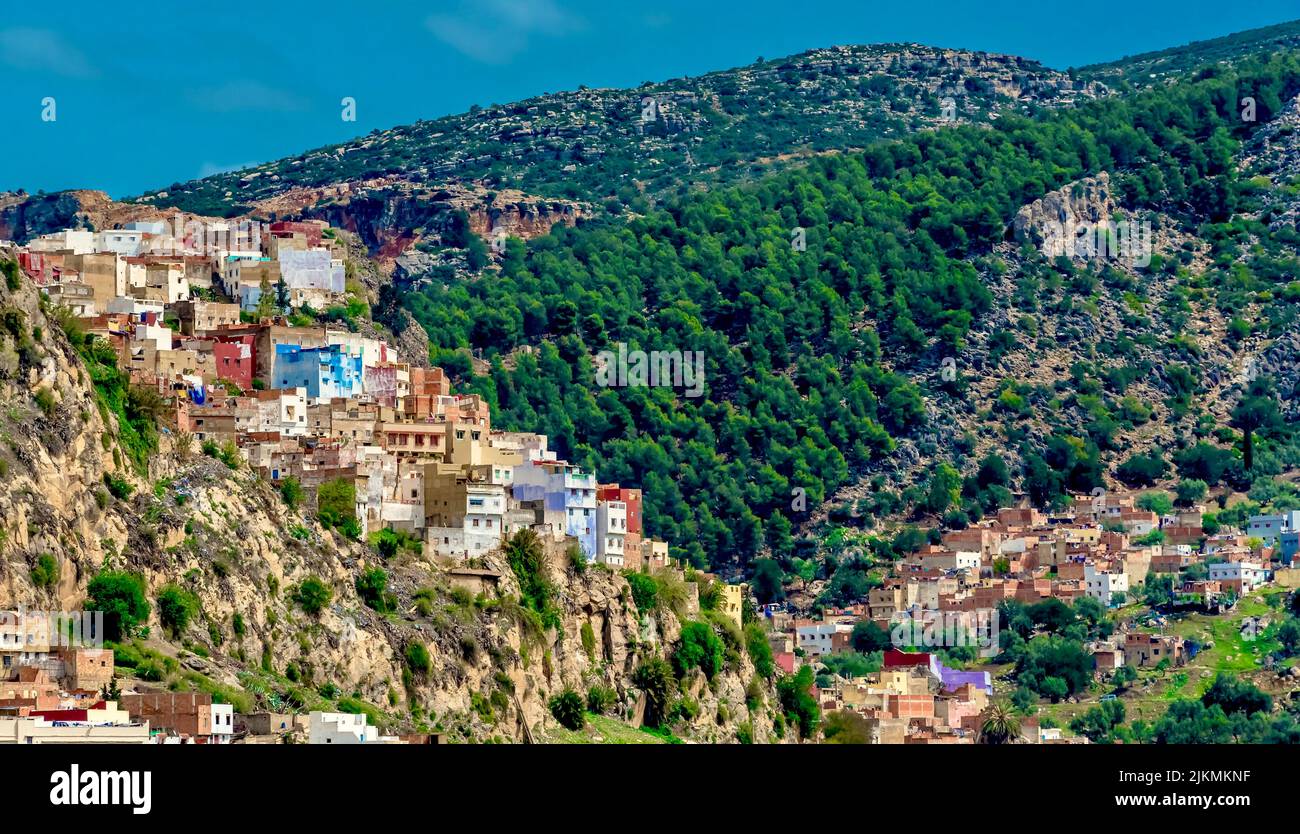 Eine kleine Stadt Häuser auf einem Felsen eines Berges mit grünen Bäumen unter blauem Himmel bedeckt Stockfoto