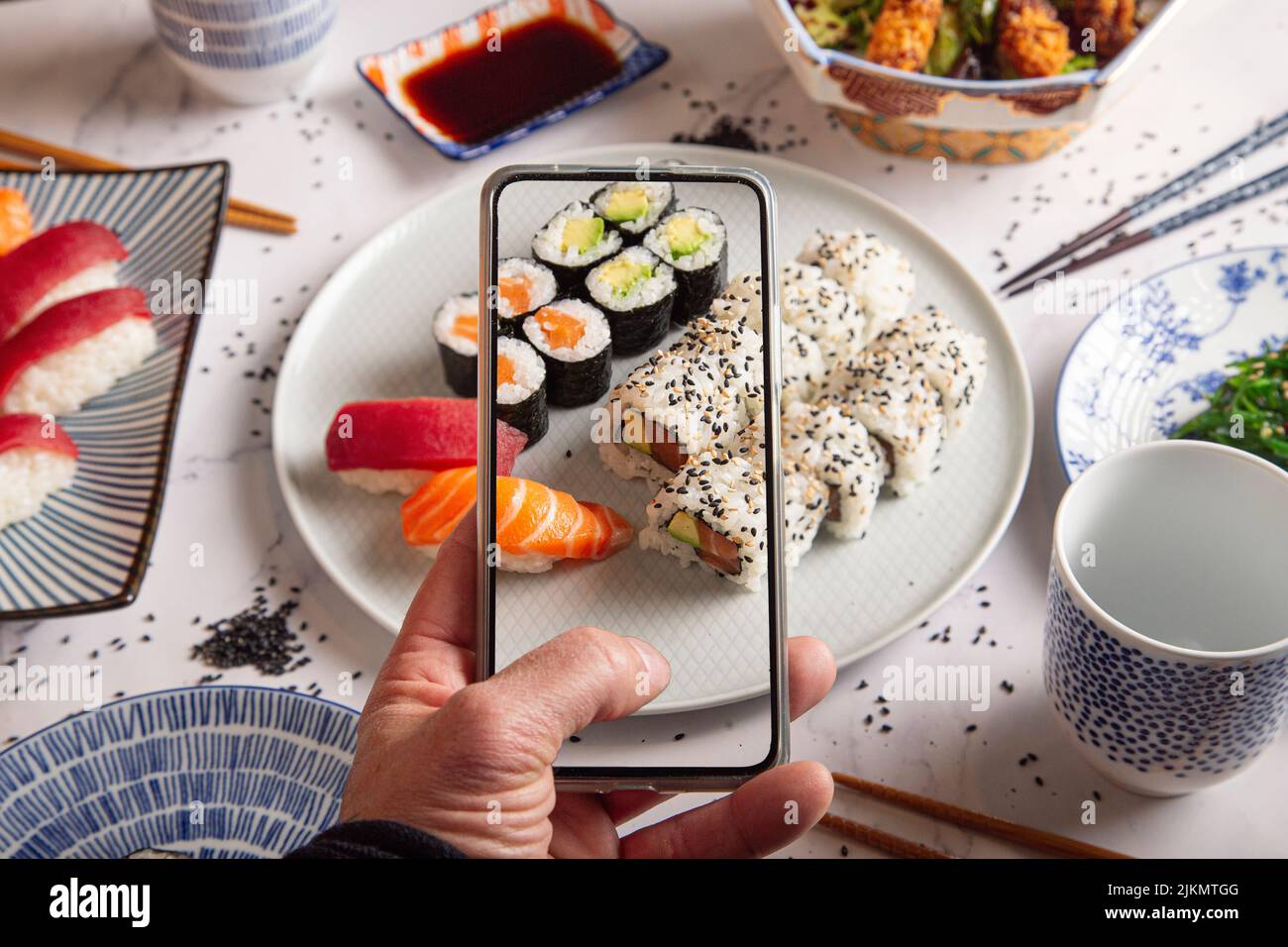 Maki-Rollen mit geräuchertem Lachsmännliche Hände fotografieren Sushi-Rollen mit dem Mobiltelefon. Draufsicht.Junge Mann, der ein Foto von einem Teller Sushi auf einem Stockfoto