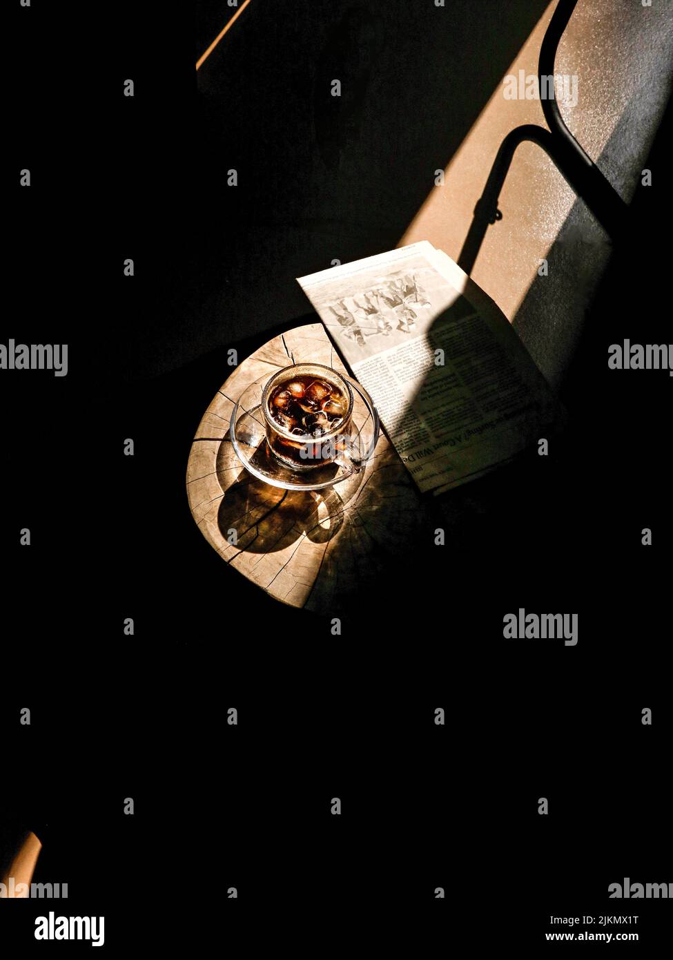 Ein ästhetischer Blick auf eine Tasse erfrischenden Eiskaffees und Zeitung auf dem Tisch bei Sonnenlicht Stockfoto