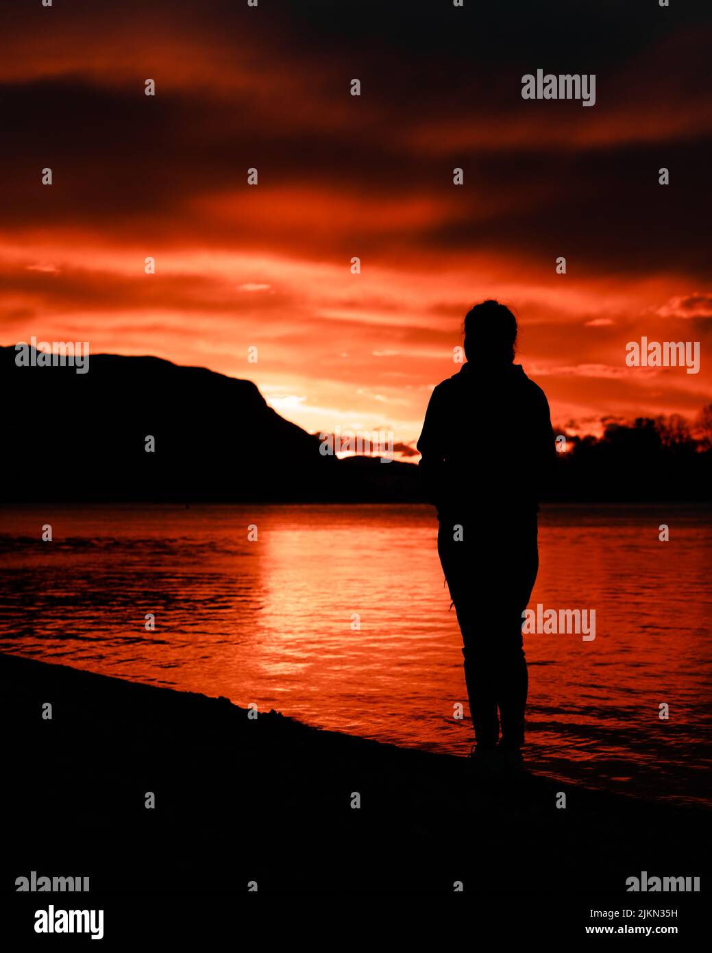 Eine Silhouette einer Person, die den Sonnenuntergang am See beobachtet Stockfoto