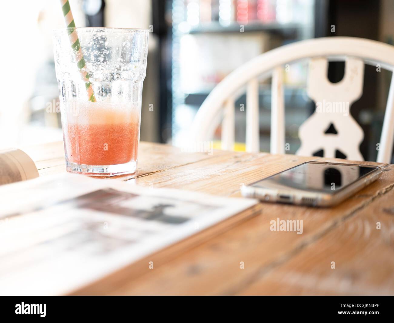 Ein Glas Smoothie mit einem Papierstroh auf einem Holztisch mit Tagebuch und Smartphone Stockfoto