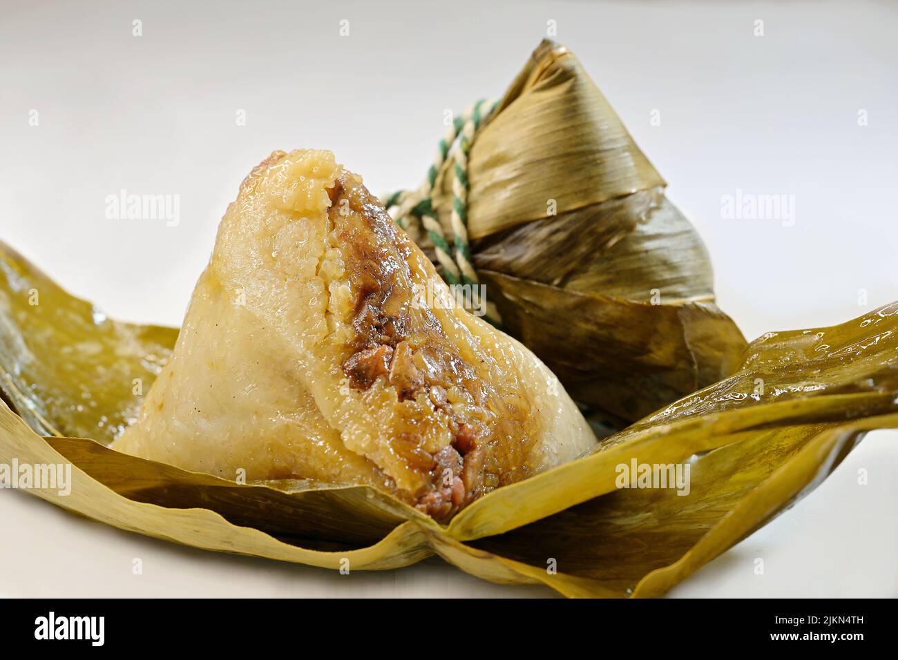 Ein chinesischer klebriger Reis, Zongzi oder Baccang, eingewickelt in Bambusblätter, und ein ungewickelter Knödel, auf weißem Hintergrund Stockfoto