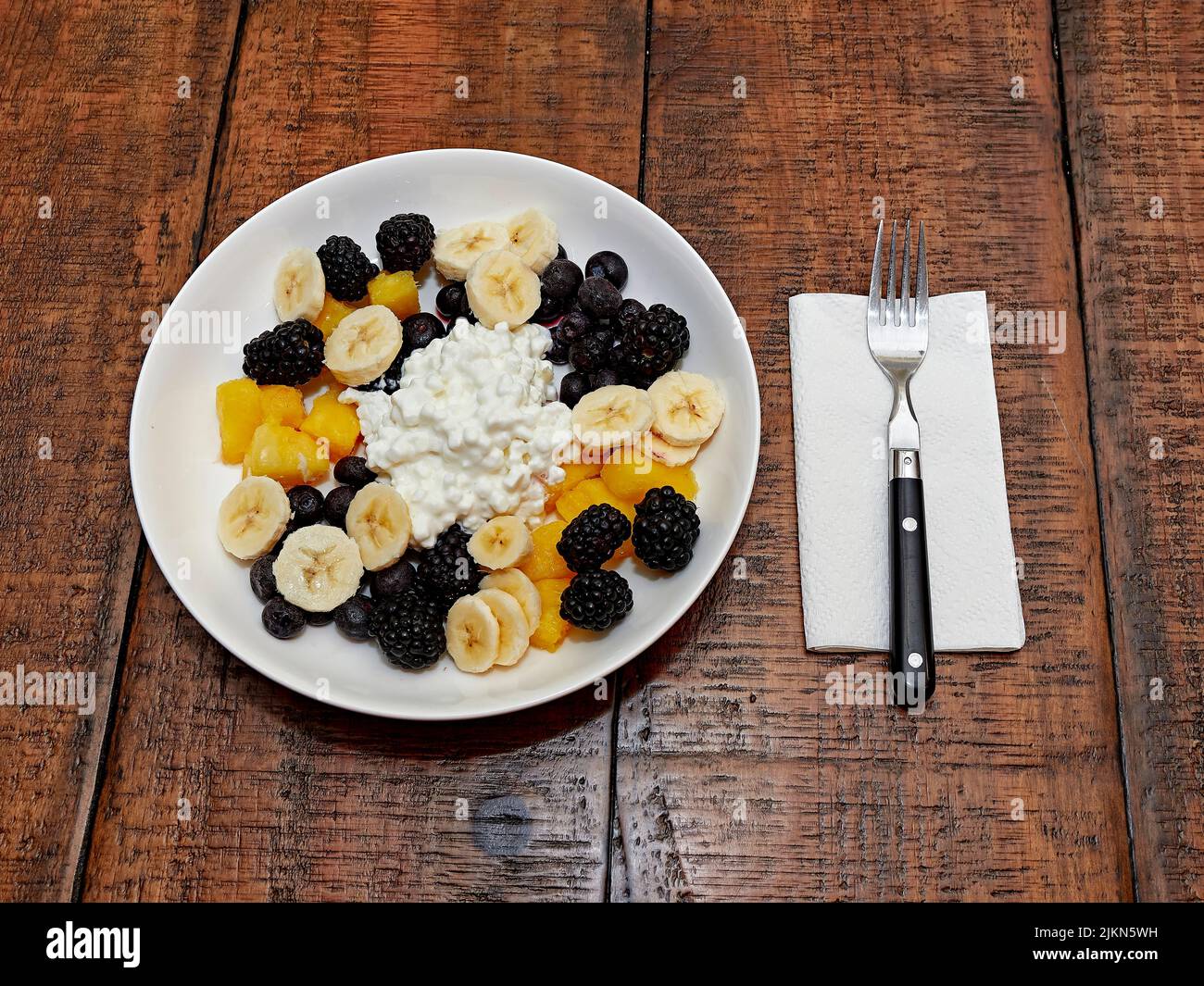 Gesunde Mahlzeit zum Frühstück oder Mittagessen Schüssel mit Quark und Obst, bestehend aus Bananenscheiben, Heidelbeeren und Brombeeren, Blick von oben. Stockfoto